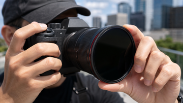 Photographer adjusting a circular variable ND filter on a mirrorless camera in bright sunlight