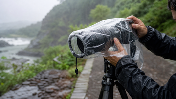 Photographer using a clear rain and dust cover on a tripod-mounted camera in rainy outdoor conditions
