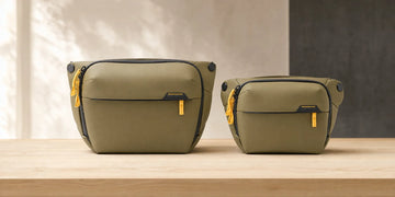 Peak Design Everyday Sling V2 6L and 3L in Kelp side by side on a wooden workbench, showing the size difference; generated illustration
