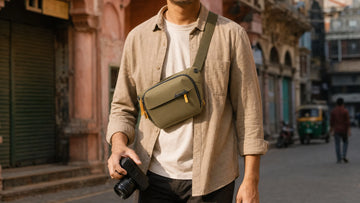 Photographer wearing the Peak Design Everyday Sling 3L across the chest on a city street, holding a compact camera; generated illustration
